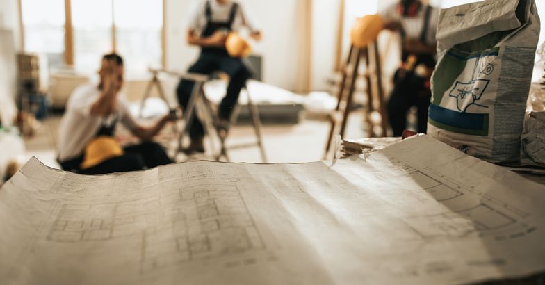 close up of blueprints at construction site with manual workers in the background