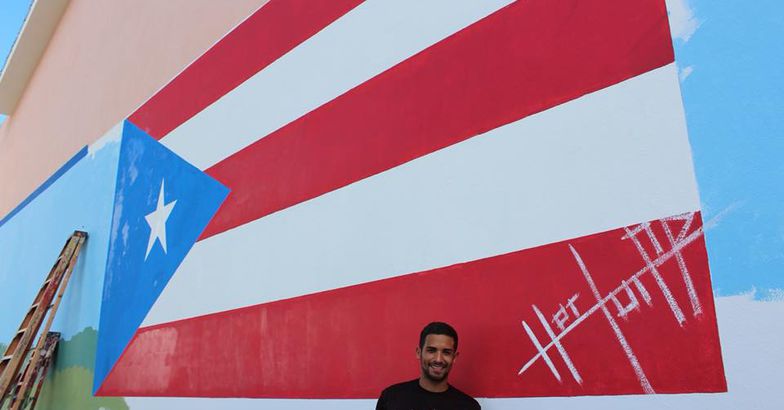 héctor collazo hernández holding paint brush standing in front of flag mural