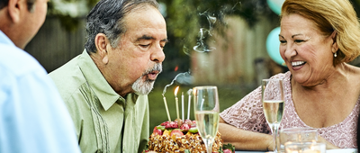 Senior woman looking at man blowing candles on birthday cake