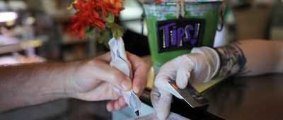 A patron uses a pen wrapped in paper to sign a credit card receipt