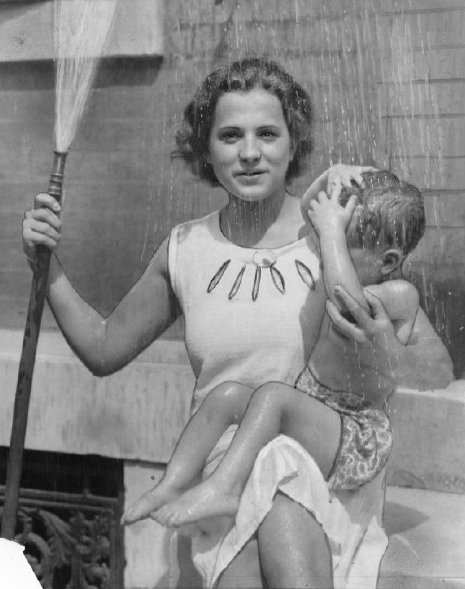 August 1, 1933: A heat wave in Philadelphia finds Marie Pergy beneath the fountain spray of a garden hose as she holds Luciell Falcone.