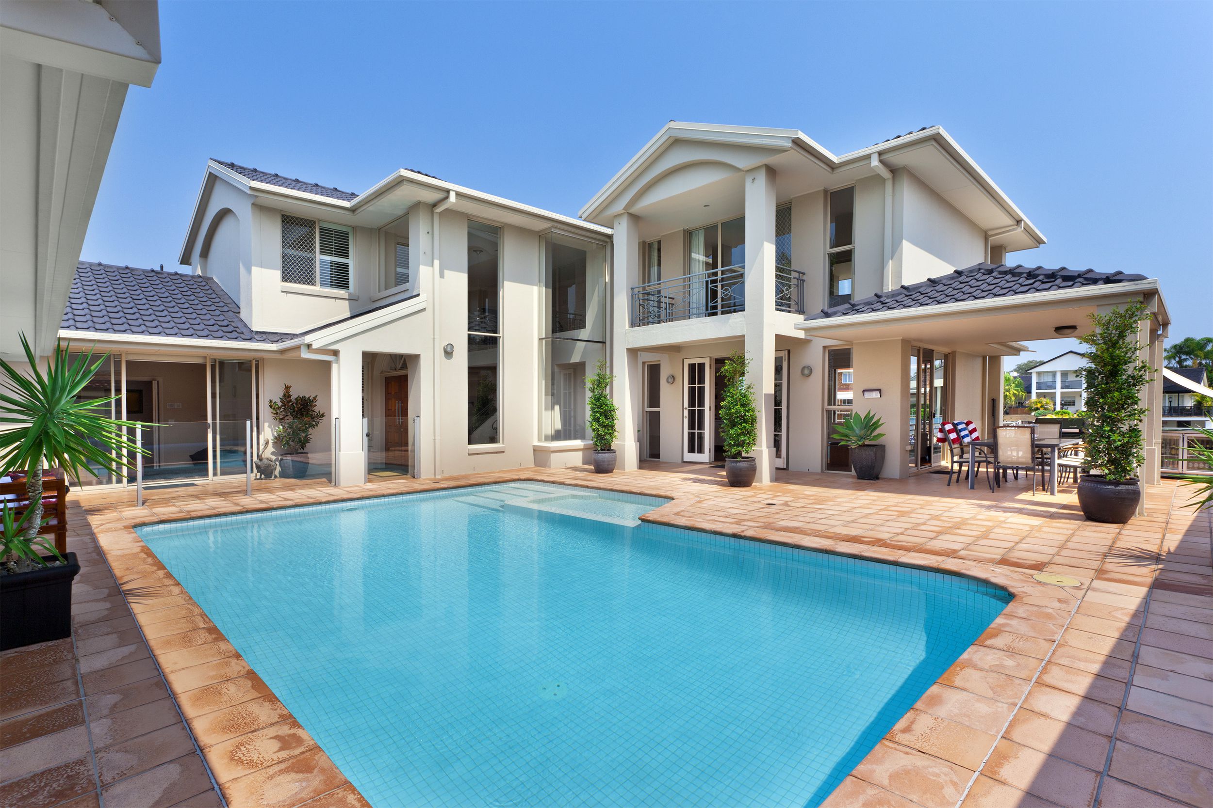 Focus on in-ground swimming pool surrounded by brick sides and large house on a sunny day