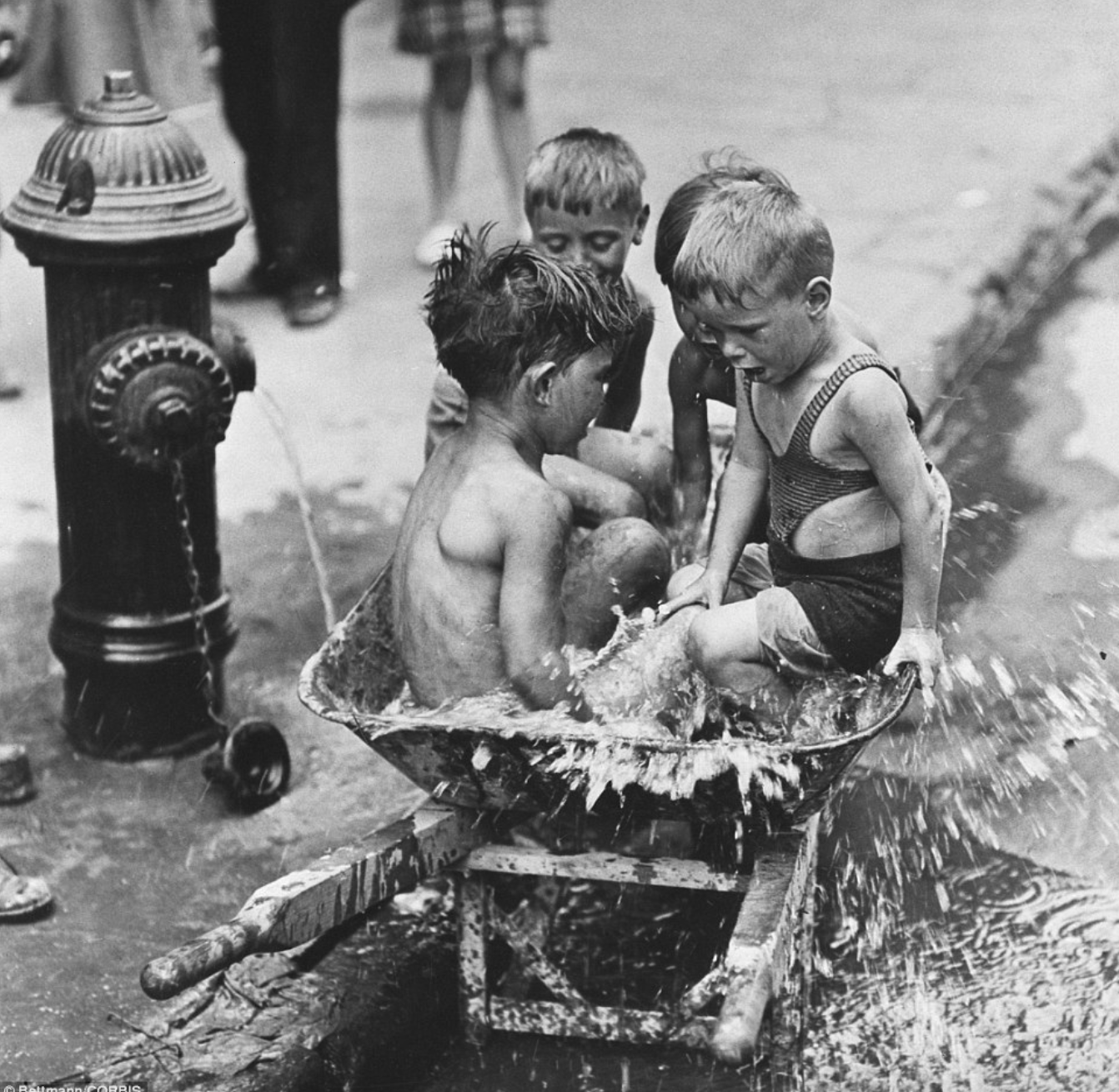 Seated in a WPA wheelbarrow beside a gushing fire hydrant on the Lower East Side, four boys cool off in 95 degree heat in 1939. [Bettmann / Corbis Archives]