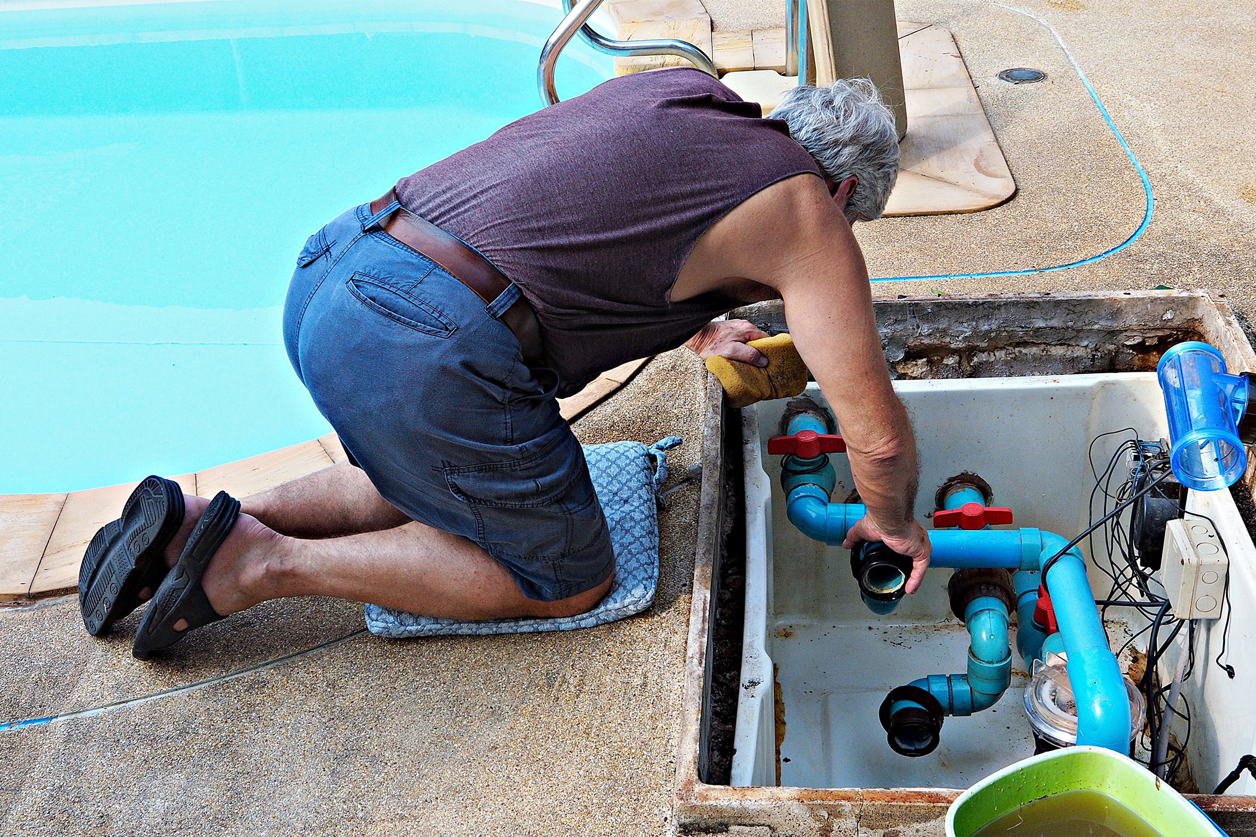 Male pool technician fixing swimming pool water pump on the side of an in-ground swimming pool