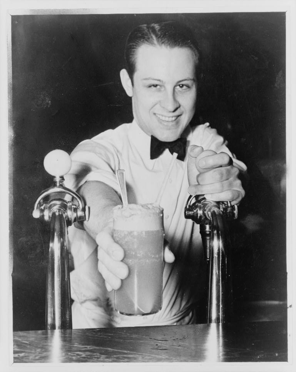 A Soda jerk passing an ice cream soda between two soda fountain. Photo by Alan Fisher 12/19/1936