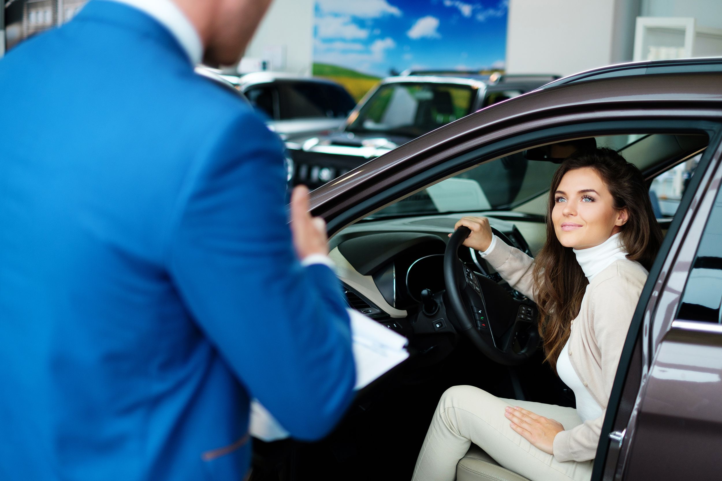Woman Is in Car in Car Dealership Showroom Looking at Male Car Dealer