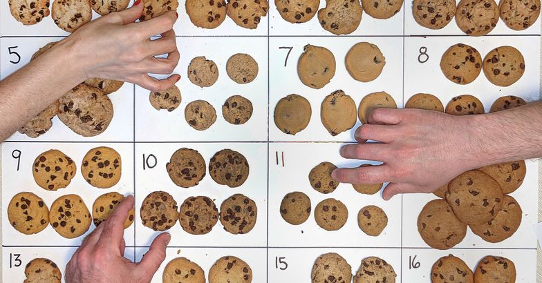 chocolate chip cookies laid out and numbered on posterboard, hands reaching for cookies