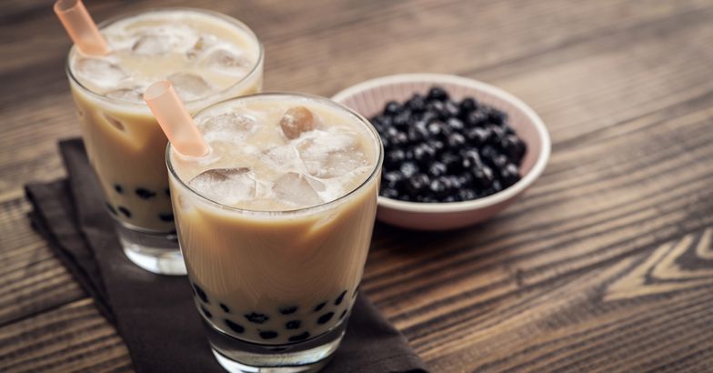 homemade boba milk tea, two glasses, with bowl of boba in background, on wooden surface