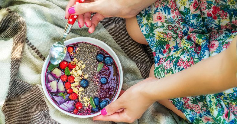 acai bowl with chia seeds and berries over blanket, held by two hands with nail polish