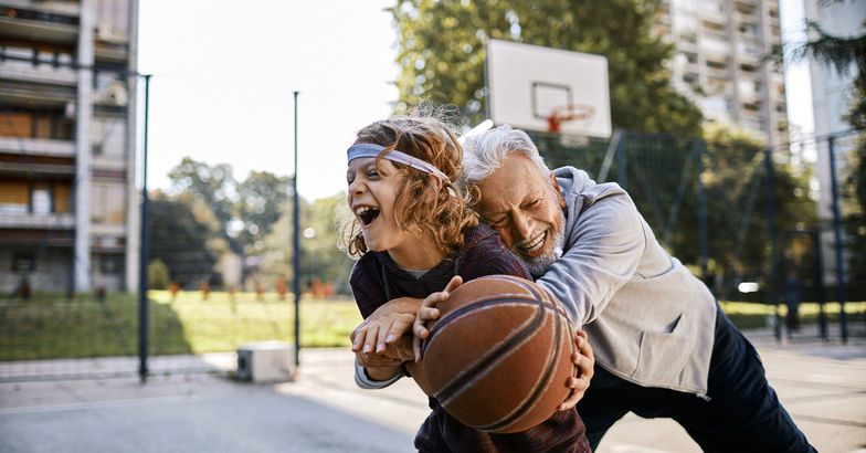 senior man hugging grandchild, playing basketball together