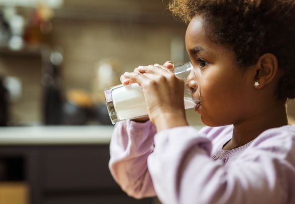 Profile view of small black girl drinking milk at home.
