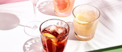 Summer cocktail with fruit and ice. Drink on white table over pink wall in sunlight with palm leaf shadow. Summer, tropical, fresh cocktail concept