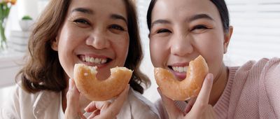 Portrait attractive beautiful two people family use cellphone take photo picture doughnut video story smiley overjoy donut at sofa couch living room have good time together quarantine social distance.