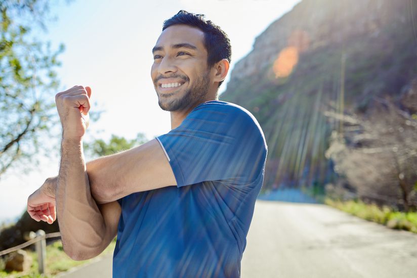 Shot of a handsome young man standing alone and stretching during his outdoor workout