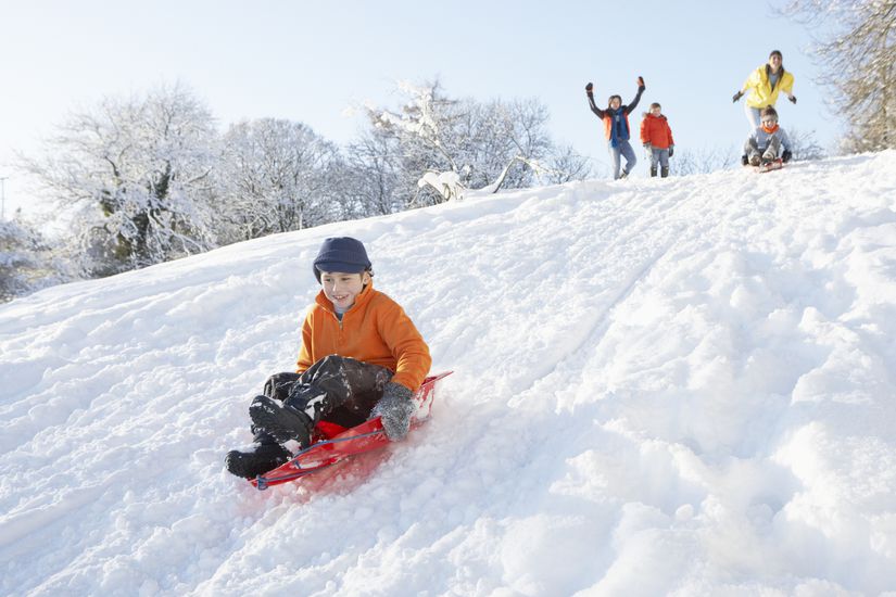 Young Boy Sledging Down Hill With Family Watching