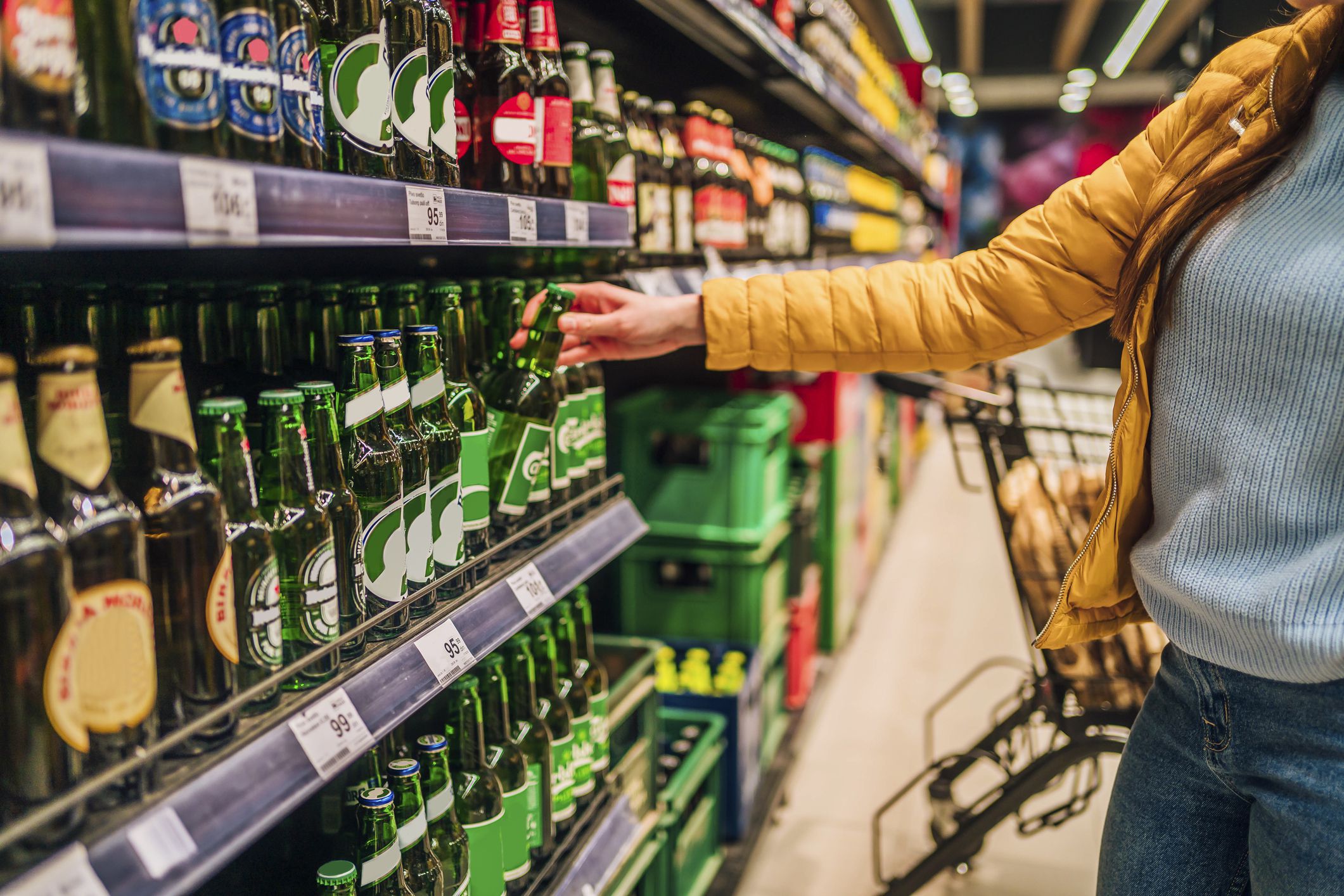 Woman customer in alcohol section in supermarket or liquor store holding a bottle from the shelf