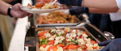 The concept of a culinary buffet dinner catering comes to life as a group of people gather in a restaurant, enjoying an all-you-can-eat spread of meat, vegetables, and other delectable food options.