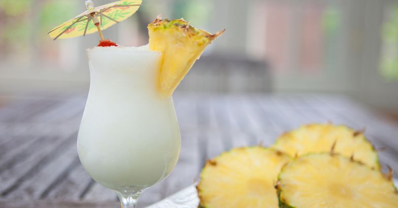 piña colada next to pineapple slices on plate on wooden table