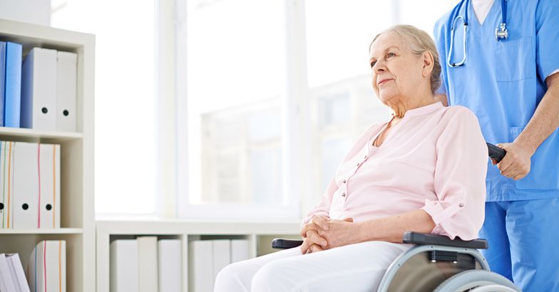 nurse pushing senior woman in wheelchair down hallway