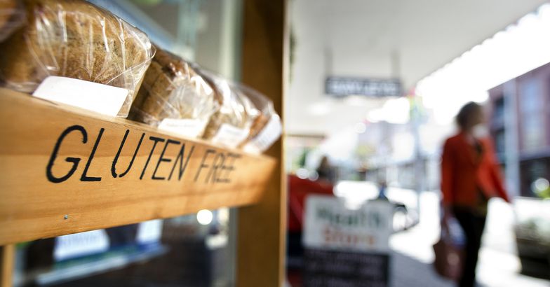 close-up of gluten-free bread shelf at grocery store, woman in distance