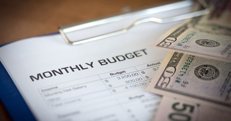 monthly budget on clipboard, $50 bills beside it