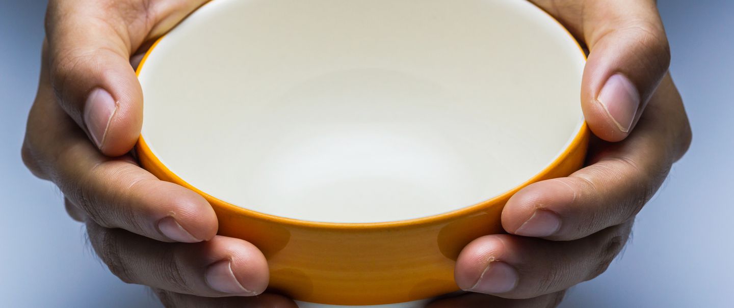 The hungry female holding an empty bowl on white background.