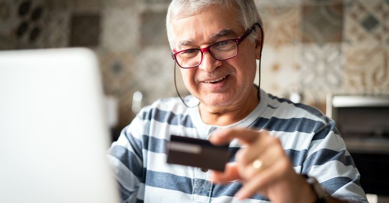 senior man holding credit card smiling with laptop open