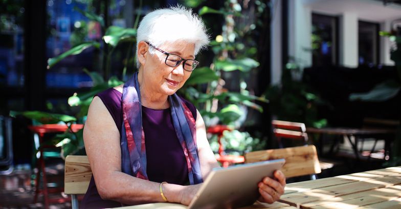 senior woman using tablet, seated at outdoor table