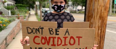 child holding cardboard sign that reads "don't be a covidiot, wear a mask"